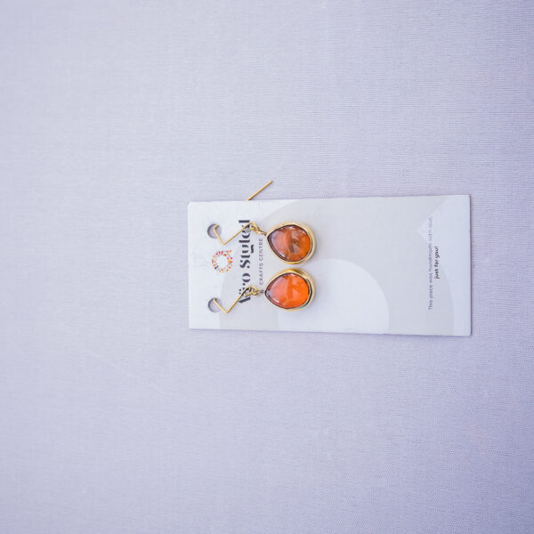 Dangling brass earrings with orange beads made from recycled glass.