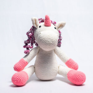 Handmade crochet unicorn soft toy in white and pink with a textured horn and curly yarn mane.