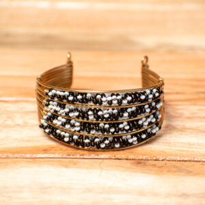 A wide, handcrafted open-cuff bracelet made of layered horizontal rows of golden brass wire, with the front section densely wrapped in alternating rows of small black and white seed beads.