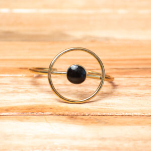 A handcrafted golden brass open cuff bracelet,featuring an integrated, large open circular frame at the center that holds a smooth, round black stone cabochon.