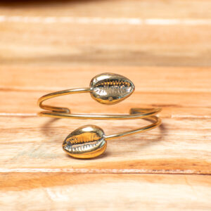 A handcrafted golden brass open wrap-around cuff bracelet, featuring two smooth parallel bands that cross over and end with a cast metallic cowrie shell on each tip.