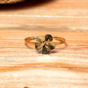 A handcrafted gold-tone brass cuff bracelet featuring a central five-petal flower with etched texturing on the petals and delicate projecting stamens.