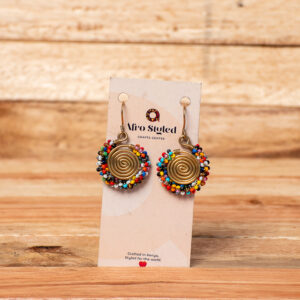 A pair of handcrafted golden brass drop earrings featuring a tightly coiled wire spiral disc, tightly bordered around the outer edge with small, vibrant seed beads in a variety of mixed colors.
