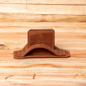A stack of brown leather square coasters with rounded corners neatly arranged inside a matching brown leather holder featuring a curved, arched strap design.