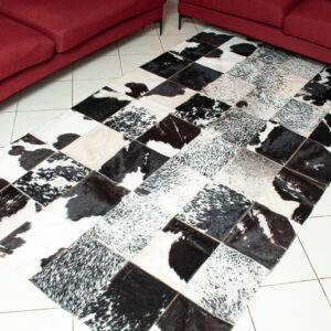Handcrafted black and white patchwork cowhide rug made from genuine cowhide leather, displayed in a modern living room.