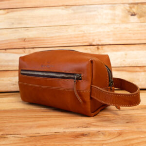 A tan leather travel toiletry bag with a front zip pocket and side handle.