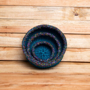 A top-down view of a set of three nested circular teal woven baskets with colorful beaded rims.