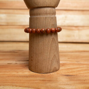 A stretch bracelet made of smooth, sparkling reddish-brown goldstone beads displayed on a wooden stand.