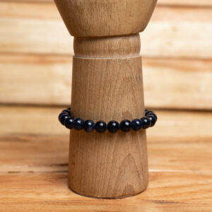 A stretch bracelet made of smooth, sparkling deep blue goldstone beads displayed on a wooden stand.