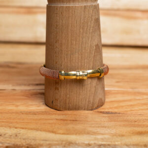 A mixed metal coiled copper and brass wire bracelet displayed on a wooden stand
