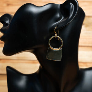 A gold-tone brass ring drop earring featuring a curved brass pendant displayed on a black mannequin stand.