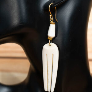 A white carved bone drop earring with vertical cutouts and a matching bone bead, displayed on a black mannequin bust.