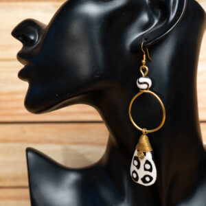 A black and white batik bone teardrop dangle earring with a brass hoop displayed on a mannequin stand
