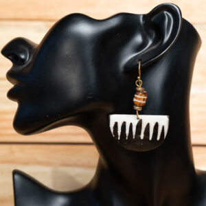 A black and white batik bone half-moon drop earring with a striped bead accent displayed on a black mannequin stand.