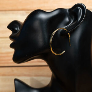A polished gold-tone brass open hoop earring displayed on a black mannequin stand.