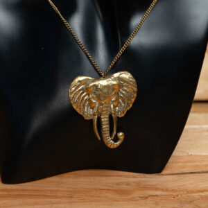 A gold-tone brass elephant head pendant on a brass chain, displayed on a black mannequin stand.