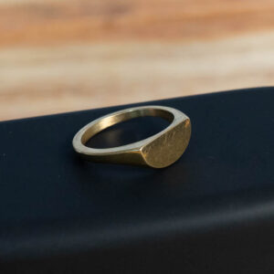 A gold-tone brass ring with a flat half-moon top face resting on a dark surface.