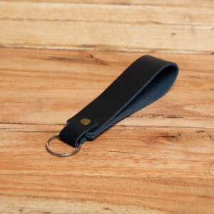 A black leather wristlet loop keychain secured with a brass rivet and silver metal split ring.